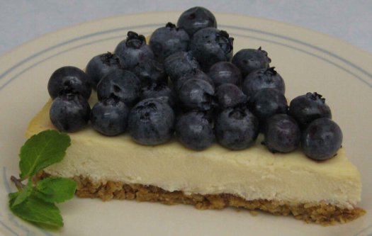 Cheesecake wedge with fresh blueberries on top, along with fresh mint to the side.