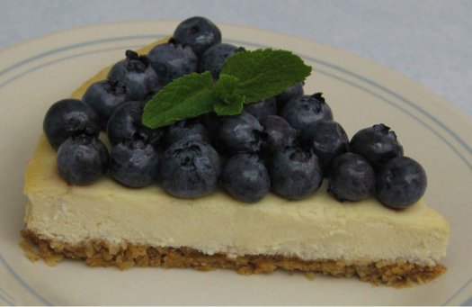 Cheesecake wedge with fresh blueberries, garnished with fresh, green mint.