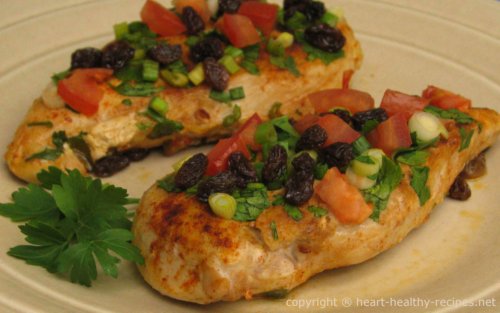Chicken Valencia topped with paprika, chopped green onions, tomatoes, and raisins. Garnished with parsley sprig.