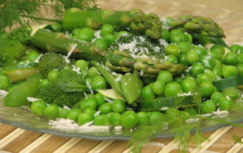 Mixed vegetables of asparagus, peas, broccoli and more with dill weed sprig in foreground also in background.