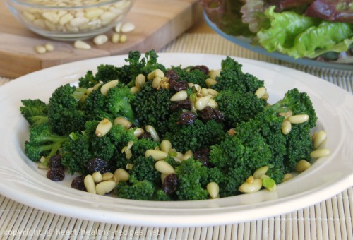 Broccoli with pine nuts and raisins along with a salad and pine nuts sprinkled in the background.