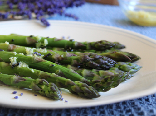 Close-up of asparagus drizzled with lemon lavender dressing and lavender bunches in background along with grated lemon zest.