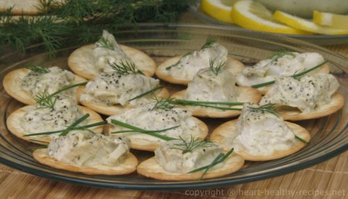 Dozen dill cod appetizers on round crackers topped with chives and dill sprigs.