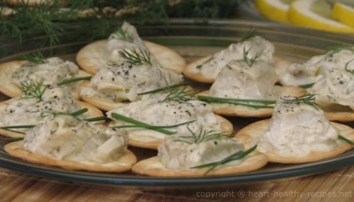 Dozen dill cod appetizers on round crackers topped with chives and dill sprigs.