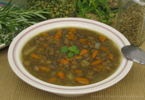 Lentil soup garnished with oregano sprig along with herbs and spices in the background.