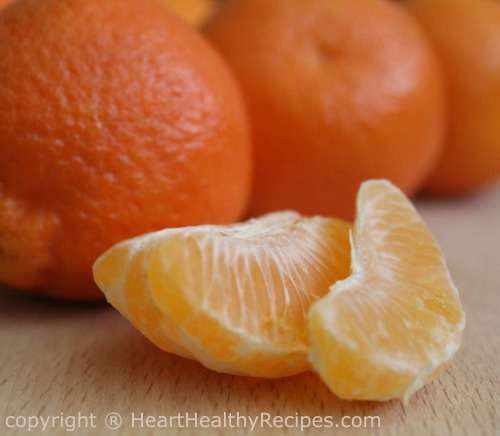 Close-up of mandarin orange slices with whole mandarin oranges in the background.