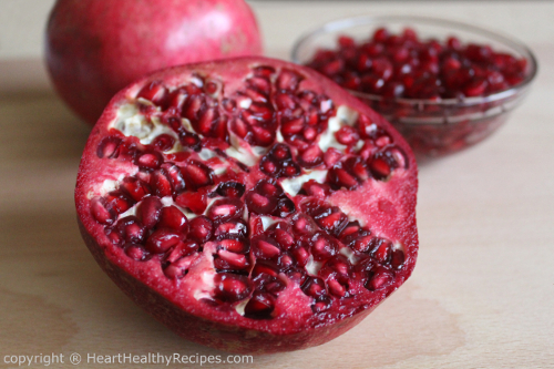 Pomegranates sliced in half with bowl of arils in the background.