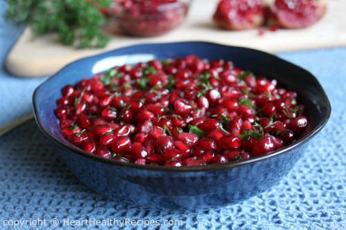 Holiday pomegranate relish with fresh parsley mixed in, along with pomegranate arils and slices in background.