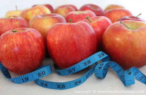 Bunch of red apples with blue measuring tape in the foreground.