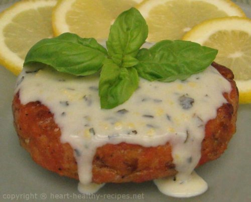 Close-up salmon cakes with dill sauce, garnished with basil sprig.