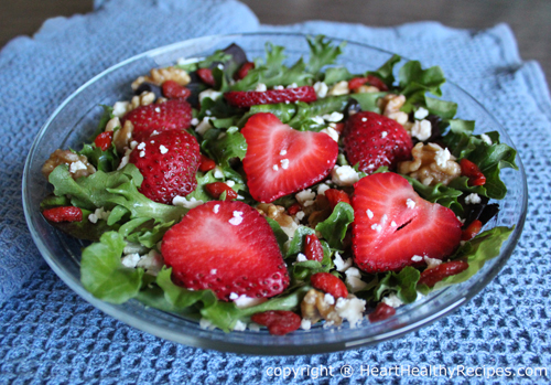 Strawberry mixed green salad with walnuts, along with goji berries on glass plate.