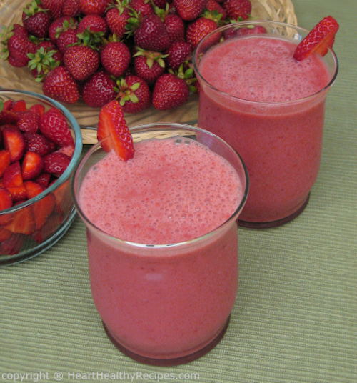 Strawberry smoothies with slices of strawberry as garnish, along with cut and whole strawberries in background.