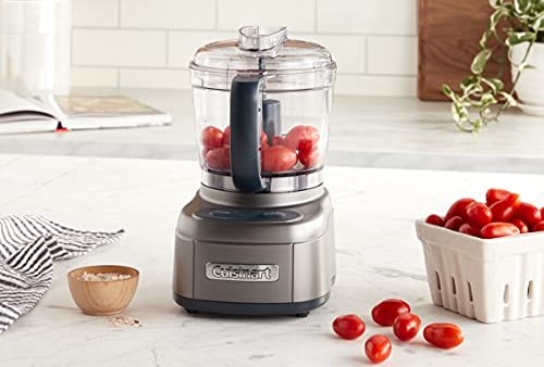 Food processor on marble countertop with red grape tomatoes.