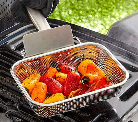 An assortment of peppers being grilled in a stainless-steel mesh grilling pan.