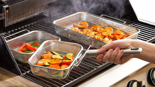 Grilled veggies and shrimp in stainless-steel mesh grilling pans on outdoor grill.