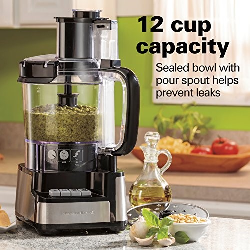 12-cup food processor filled with food along with oil and garlic herbs in foreground.