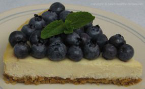 Cheesecake wedge with fresh blueberries on top, along with fresh mint to the side.