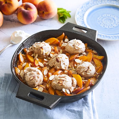 Black, medium-sized, cast iron skillet with peach cobbler and vanilla ice cream on a light blue tablecloth.