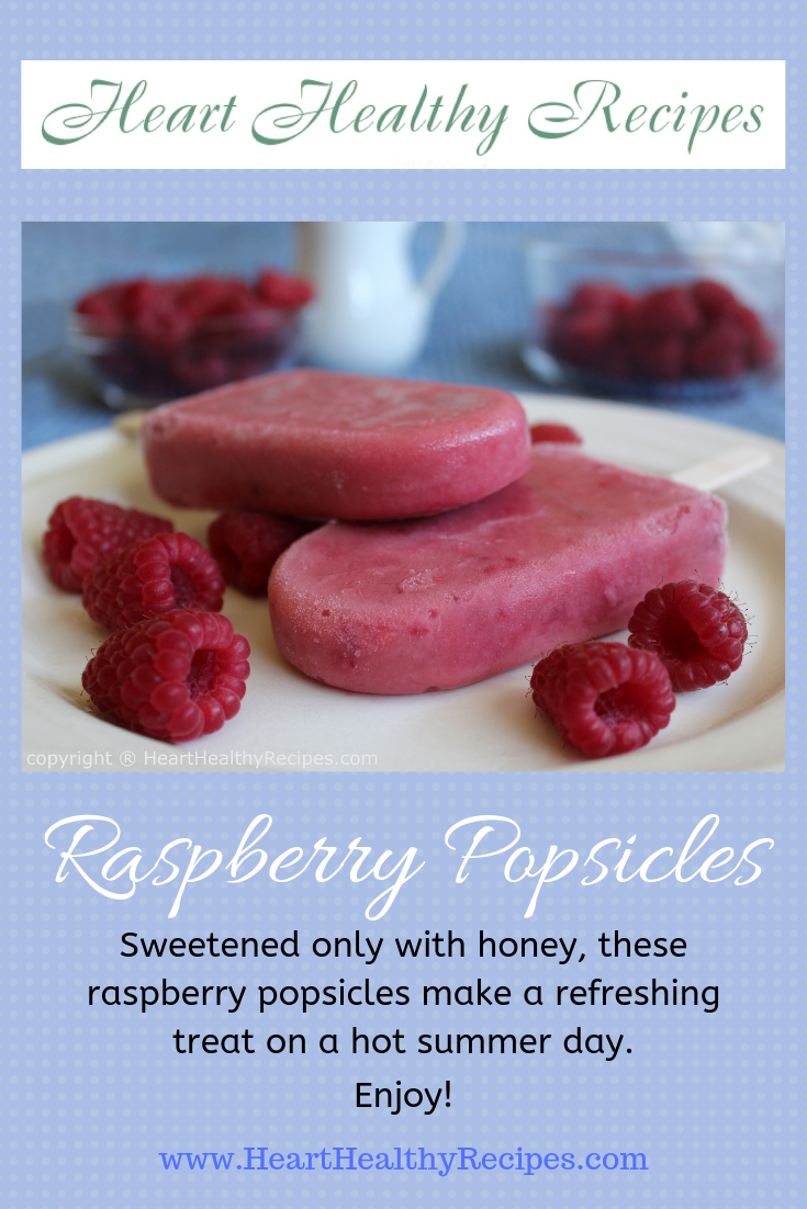 Two raspberry popsicles with several individual raspberries in foreground and more raspberries in background.