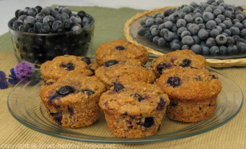 Seven whole blueberry muffins with blueberries in background.