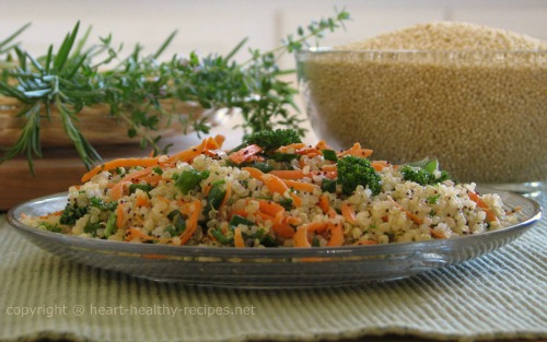 Carrot quinoa pilaf on serving plate with herbs and quinoa in background.