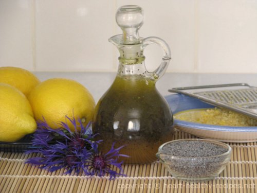 Honey poppy seed dressing with whole lemons, grated lemon zest and poppy seeds in foreground.