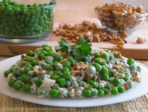 Salad with walnuts and green peas topped with parsley, along with whole green peas and walnuts in the background.