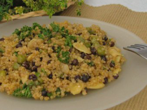 Close-up of almond-orange quinoa on serving plate with herbs in background.