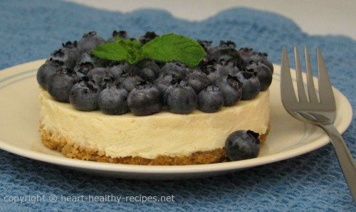 Round designed cheesecake serving topped with fresh blueberries and mint.