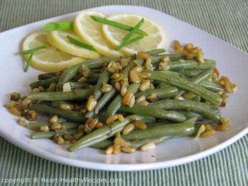 Green beans on serving plate with pine nuts, lemon and green onions.