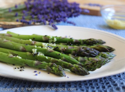 Asparagus drizzled with lemon lavender dressing and lavender bunches in background along with grated lemon zest.