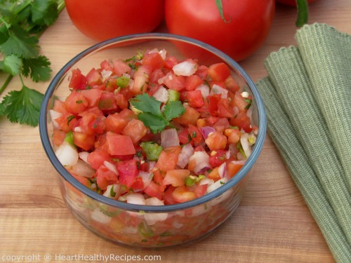 Spicy homemade tomato salsa with fresh, whole tomatoes and cilantro in background.