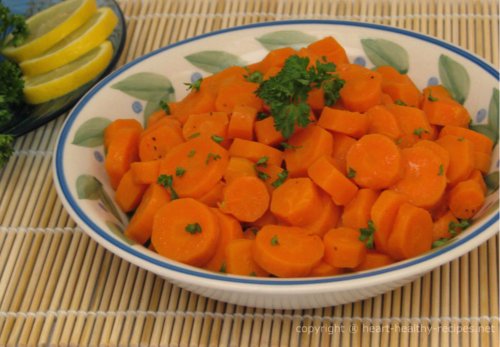Cooked sliced carrots garnished with parsley and lemon wedges in background.