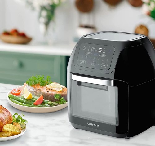 Chefman Multifunctional Digital Air Fryer displayed on marble counter with pleasant kitchen background and tasty seafood and cooked chicken on plates.