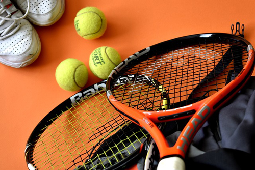 Tennis balls on orange background, along with shoes and rackets.