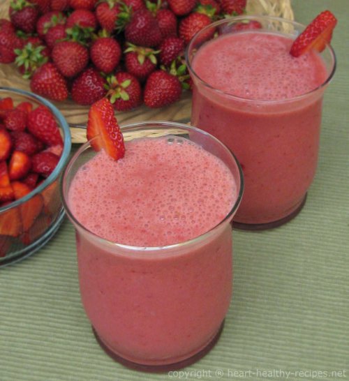 Strawberry smoothies with slices of strawberry as garnish, along with cut and whole strawberries in background.