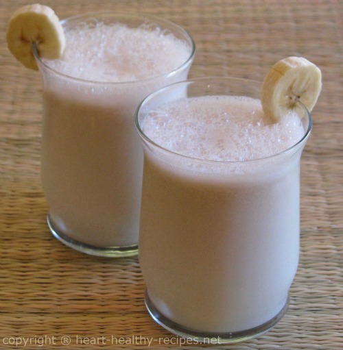 Two banana smoothies with banana slice on edge of each glass.