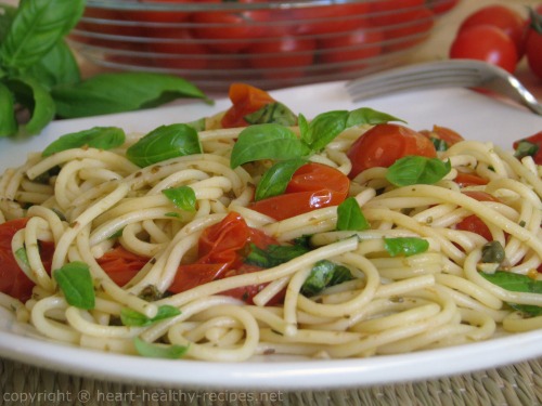 Cooked spaghetti noodles on serving plate with roasted tomatoes and chopped basil, garnished with basil.