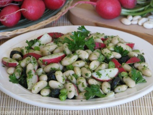 White bean salad with radishes, black olives, green onions, along with parsley-including parsley garnish on top.